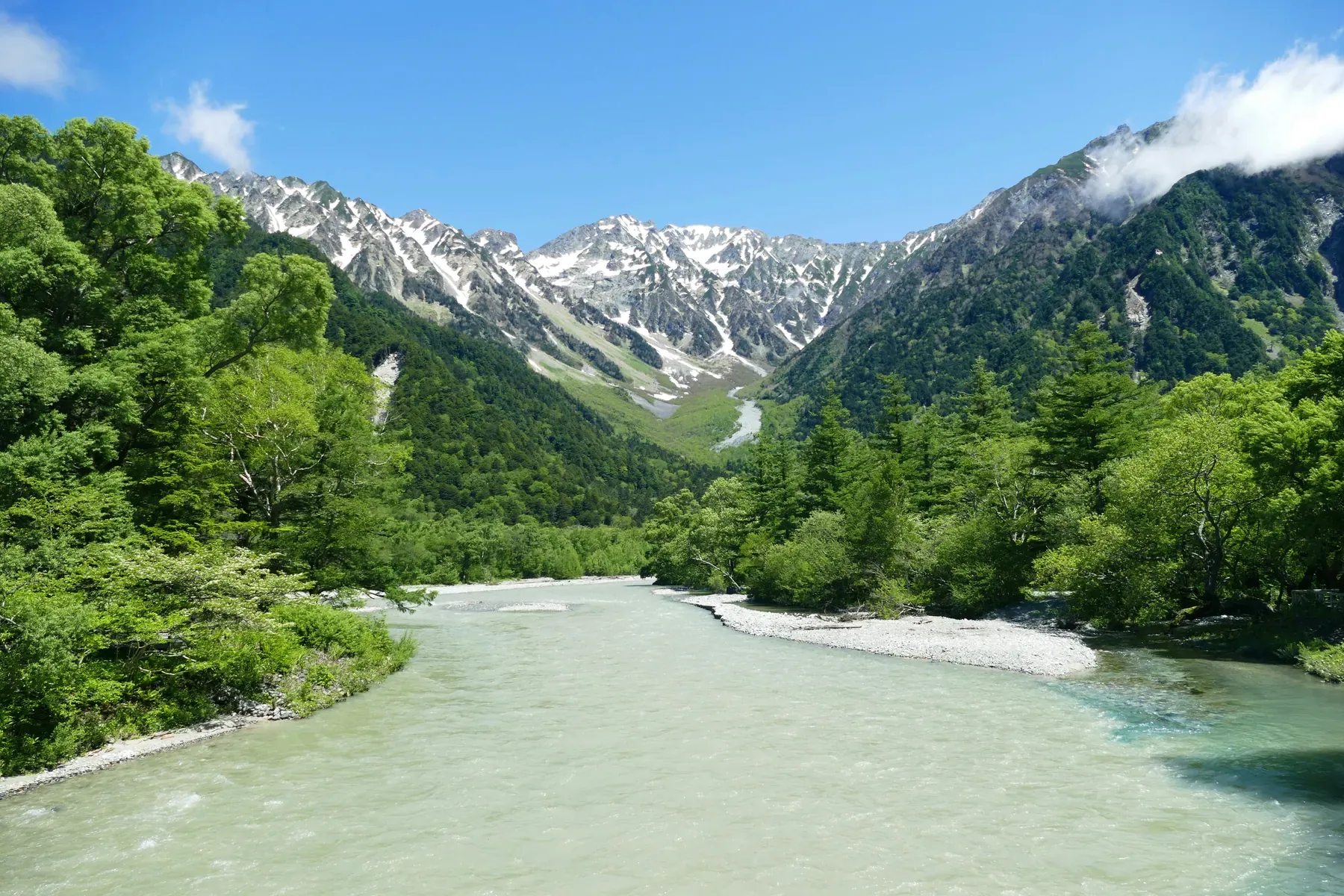 Kamikochi's river and green forest with snow-covered mountains beyond