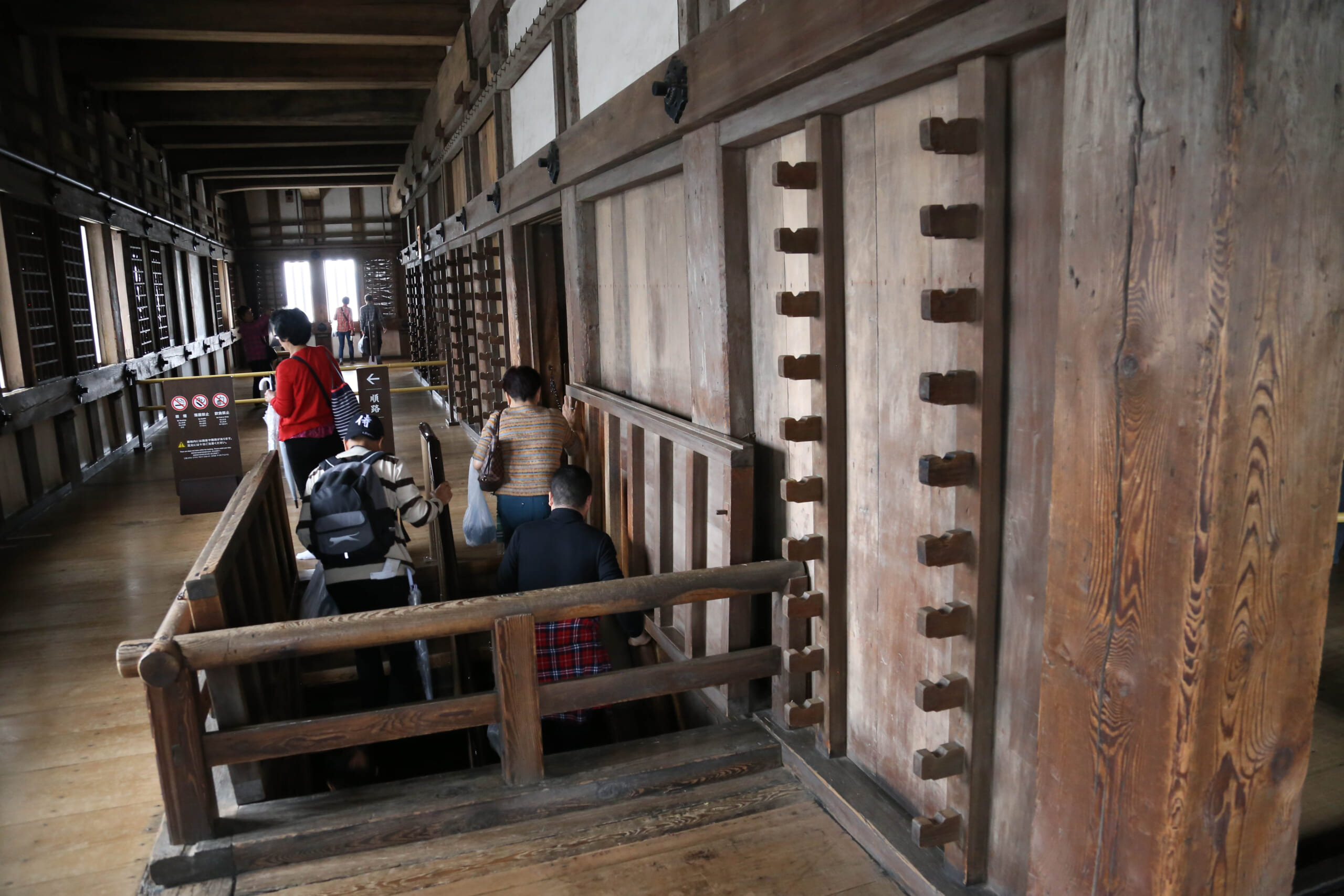 Visitors holding the handrails while descending wooden stairs inside Himeji Castle's keep