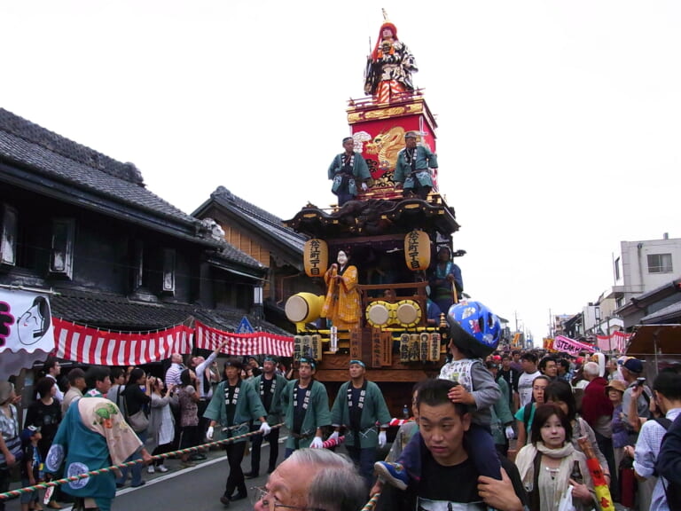 A decorated float carrying a dragon deity moves through crowds at Kawagoe Festival