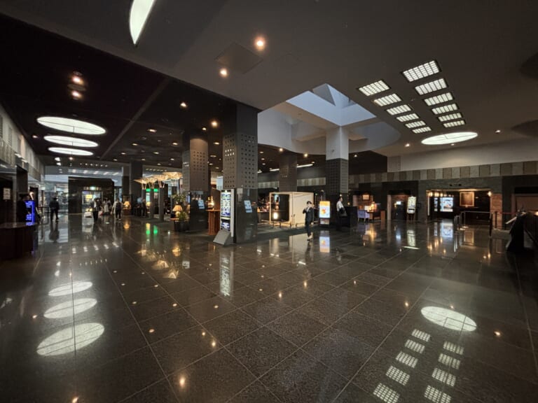 The spacious lobby of Hotel Granvia Kyoto, with ceiling lights reflected in the floor and information displays beyond