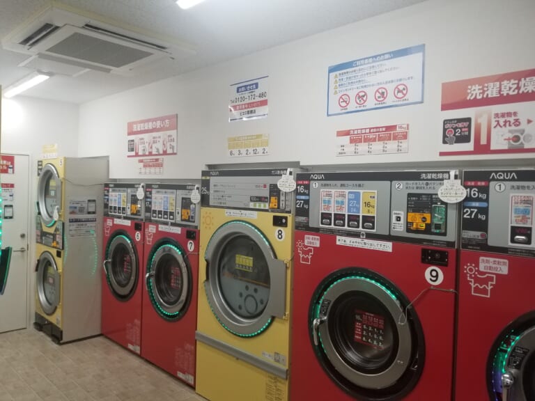 Washer-dryers and a large dryer in a Japanese self-service laundry, with instructions above the machines
