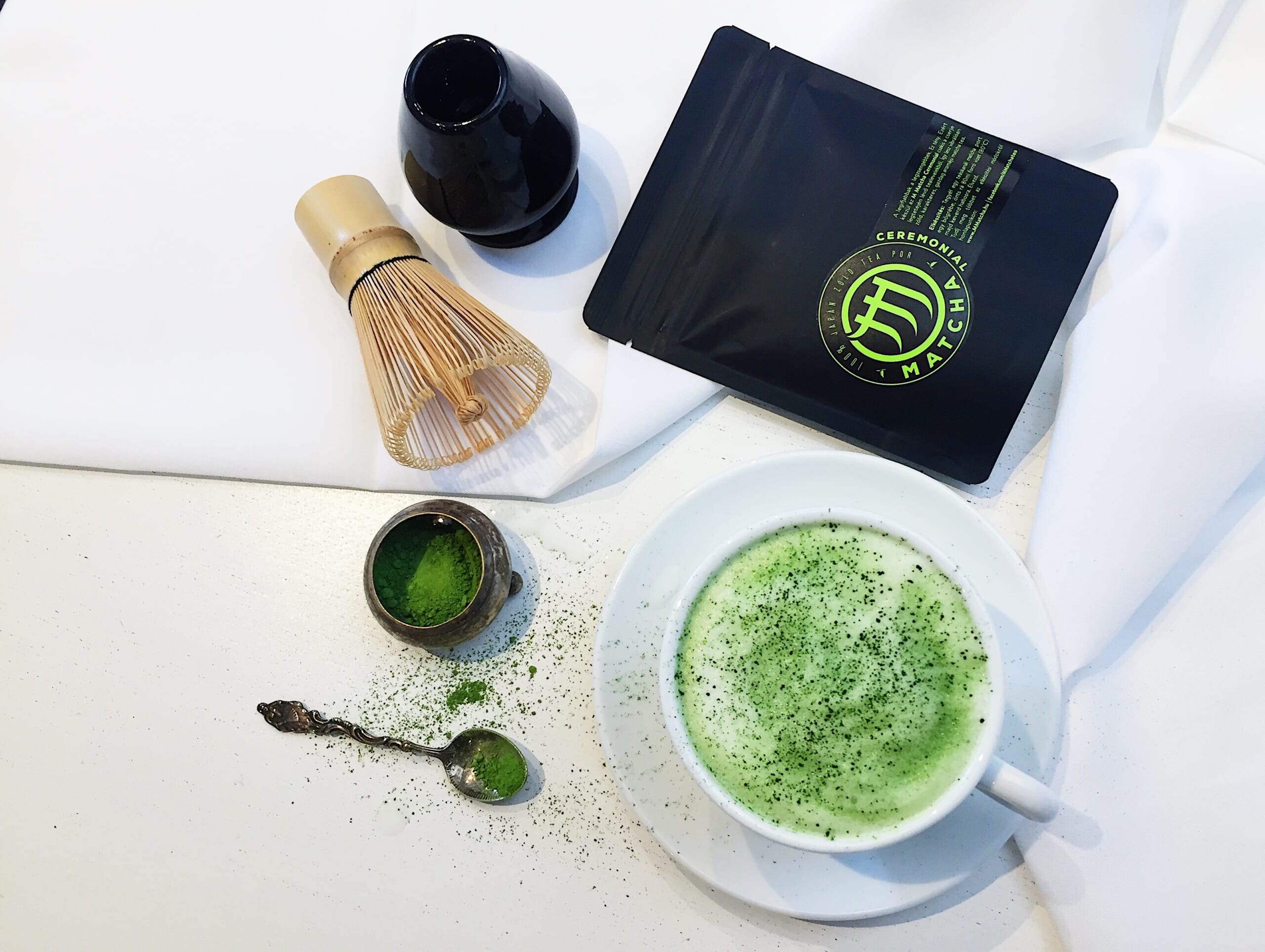 An overseas packet marked CEREMONIAL MATCHA beside a bamboo whisk and a drink made with matcha