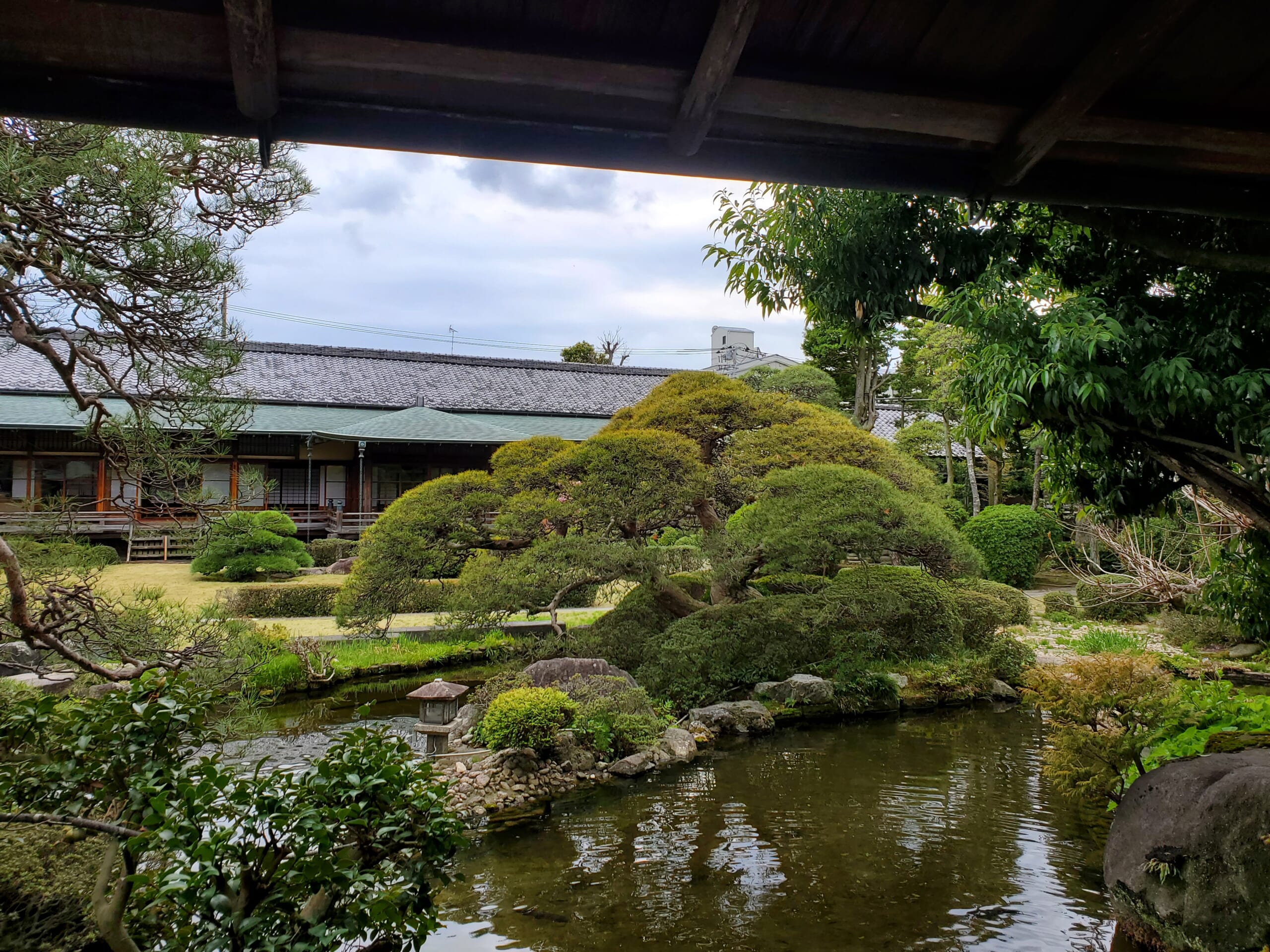 The pond and clipped planting at Suikeien Garden, with a wooden corridor on the far side