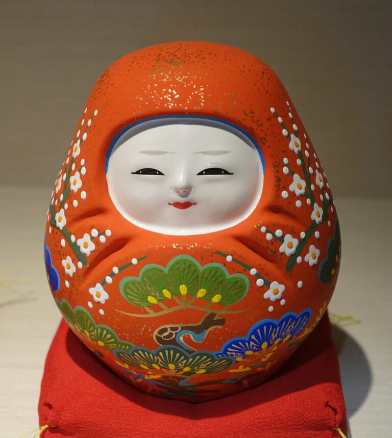 A red Kaga Hachiman roly-poly doll on display