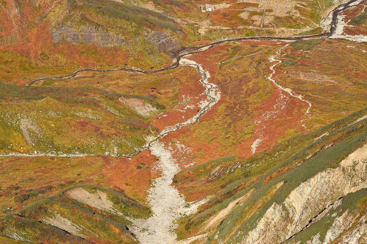 Red and golden alpine vegetation in a Tateyama valley with a mountain hut beyond