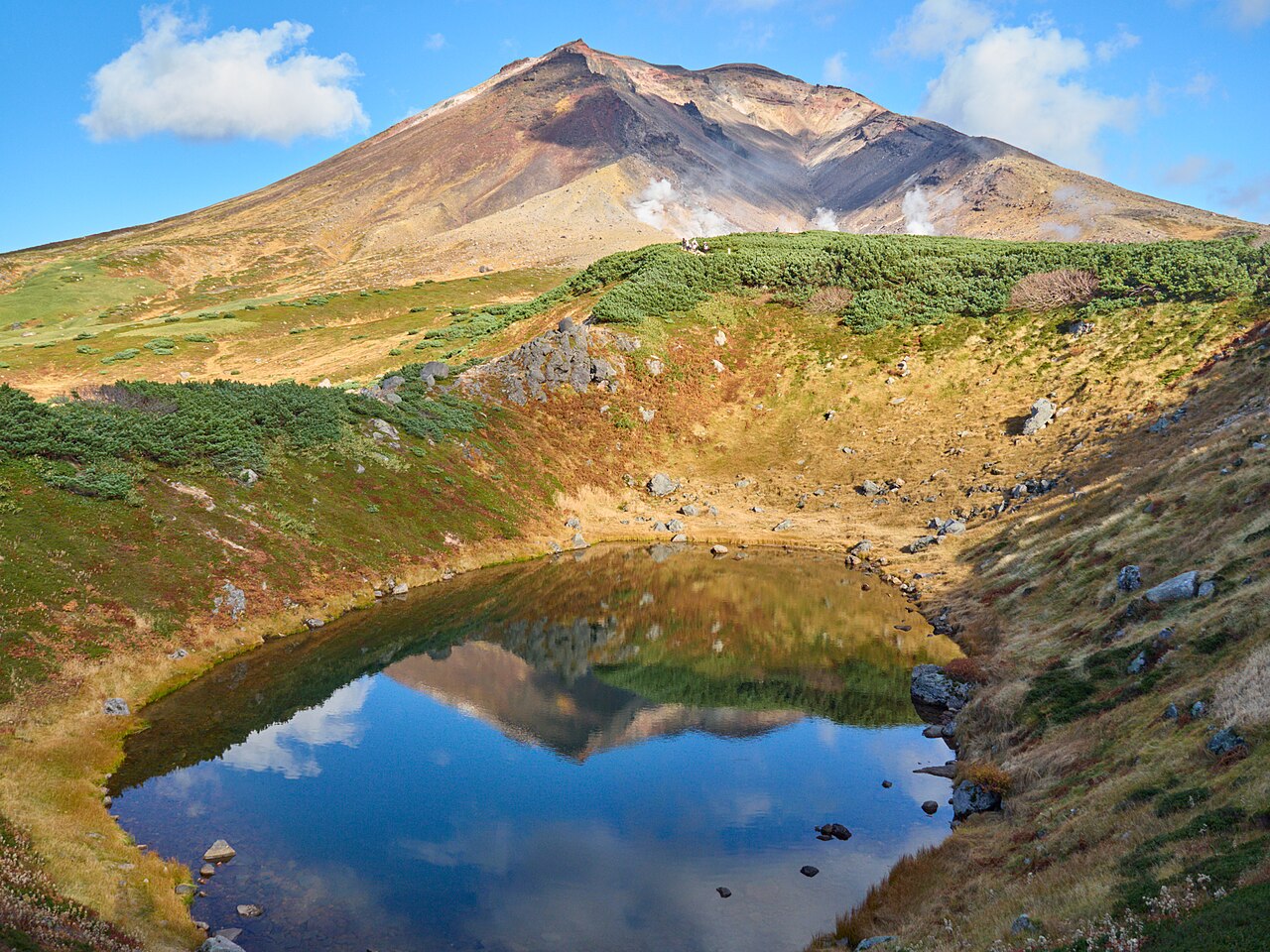 An alpine pond reflecting Asahidake and steam rising from its slopes