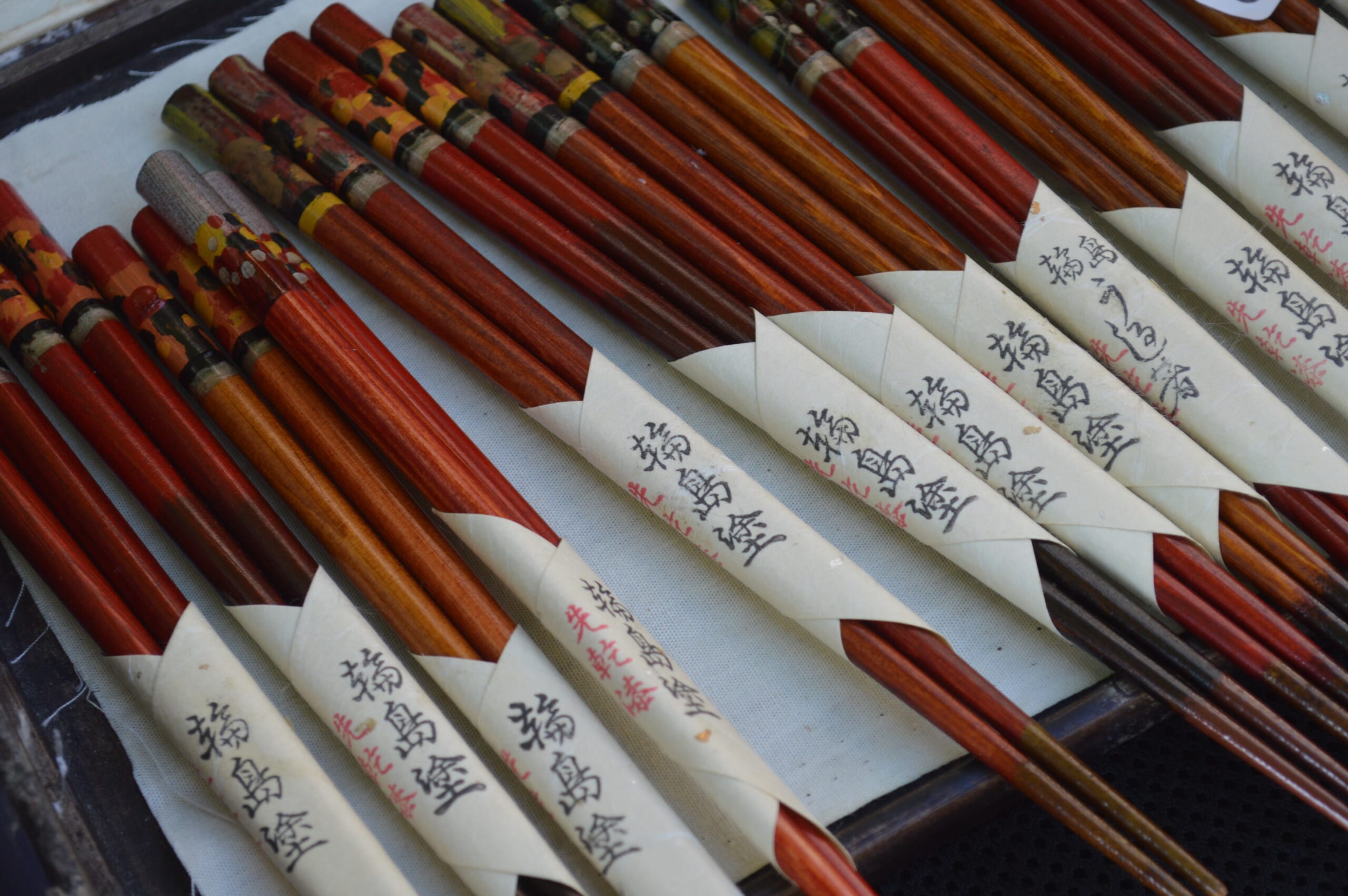 Red-brown Wajima lacquer chopsticks bundled in paper bands, with floral decoration on the handles